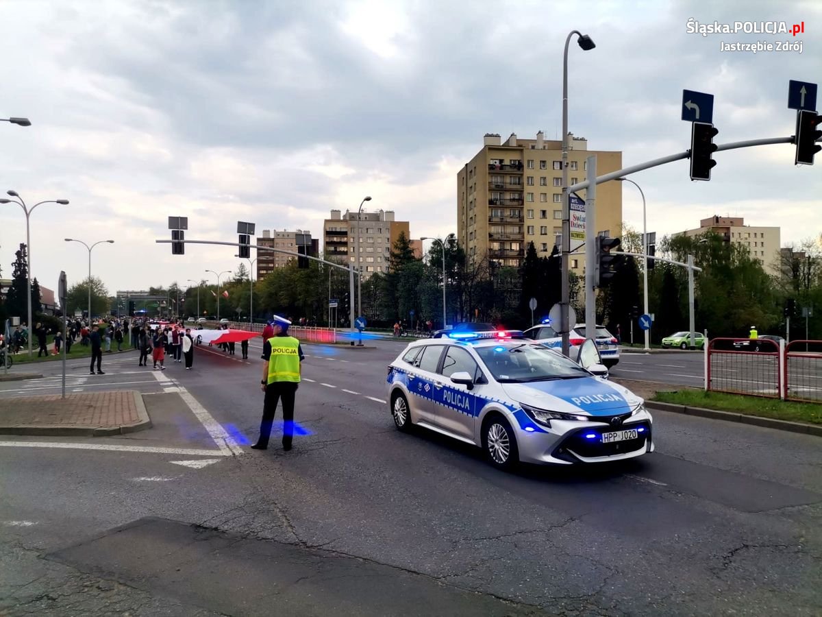 Zdjęcie policjanta ruchu drogowego, radiowozu oraz osoby niosące flagę.