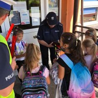 Zdjęcie kolorowe, przedstawiające policjantów i dzieci przed szkołami.