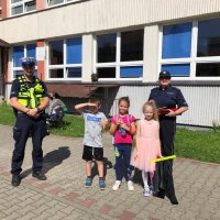 Zdjęcie kolorowe, przedstawiające policjantów i dzieci przed szkołami.