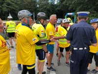 Zdjęcie kolorowe, przedstawiające policjanta i osoby uczestniczące w rajdzie rowerowym.