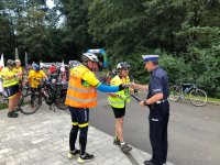 Zdjęcie kolorowe, przedstawiające policjanta i osoby uczestniczące w rajdzie rowerowym.