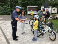 Zdjęcie kolorowe, przedstawiające policjanta i osoby uczestniczące w rajdzie rowerowym.