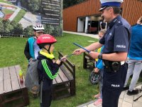 Zdjęcie kolorowe, przedstawiające policjanta i osoby uczestniczące w rajdzie rowerowym.