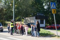 Zdjęcie kolorowe, przedstawiające policjanta ruchu drogowego i dzieci z klasy pierwszej.