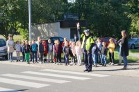 Zdjęcie kolorowe, przedstawiające policjanta ruchu drogowego i dzieci z klasy pierwszej.