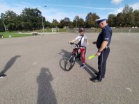 Zdjęcie kolorowe, przedstawiające policjanta ruchu drogowego i dzieci zdające kartę rowerową.