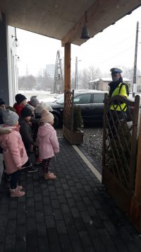 Zdjęcie kolorowe, przedstawiające policjanta ruchu drogowego rozmawiającego z przedszkolakami.