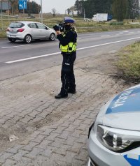 Zdjęcie kolorowe, przedstawiające policjantkę dokonującą pomiaru prędkości.