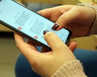 Zdjęcie kolorowe, przedstawiające ręce kobiety, która przegląda ogłoszenia przez telefon.