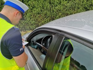 Zdjęcie przedstawiające policjanta oraz osobę otrzymującą mandat za popełnione wykroczenia.