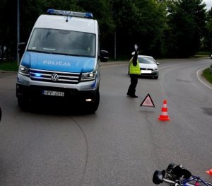 Zdjęcie przedstawiające radiowóz, policjantkę kierującą ruchem oraz uszkodzony rower.