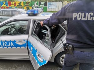 Zdjęcie przedstawiające policjanta stojącego przy radiowozie.