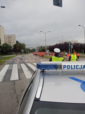 Zdjęcie przedstawiające zabezpieczających policjantów, radiowóz oraz uczestniczki biegu.