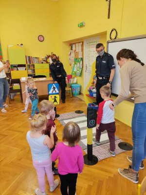 Zdjęcie przedstawiające policjantów i dzieci uczące się korzystania z przejścia dla pieszych.