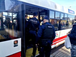 Zdjęcie kolorowe, przedstawiające policjantów w trakcie wchodzenia do autobusu.