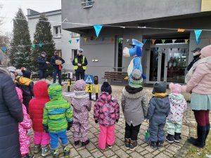 Zdjęcie przedstawiające Sznupka, który pokazuje przedszkolakom jak przechodzić przez przejście dla pieszych.