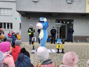 Zdjęcie przedstawiające Sznupka, który pokazuje przedszkolakom jak przechodzić przez przejście dla pieszych.