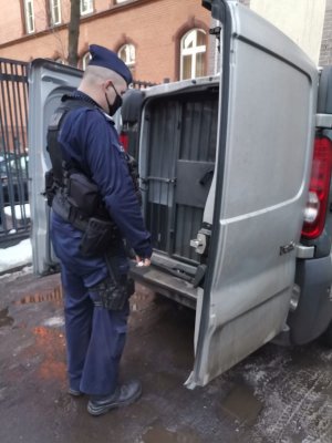 Zdjęcie policjanta stojącego przy osobie zatrzymanej.