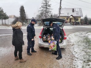 Zdjęcie przedstawiające policjantów oraz pracownika OPS-u w trakcie wyjmowania paczki z radiowozu.