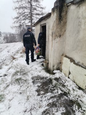 Zdjęcie przedstawiające policjantów i pracownika w momencie wejścia do domu osoby bezdomnej.