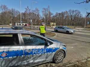 Zdjęcie przedstawiające policjanta ruchu drogowego w rejonie przejścia dla pieszych oraz radiowóz.