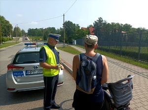 Zdjęcie przedstawiające policjanta stojącego przy radiowozie oraz rowerzystę.