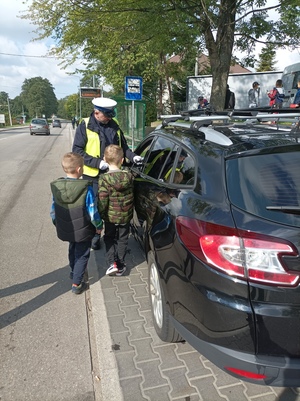 Zdjęcie przedstawiające dzieci oraz policjanta oraz kontrolowany pojazd.