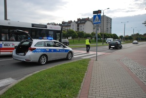 Zdjęcie przedstawiające policjanta oraz radiowóz policyjny na miejscu zdarzenia drogowego.