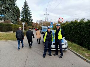 Zdjęcie kolorowe przedstawiające policjantów pilnujących porządku na drodze dojazdowej do cmentarza.