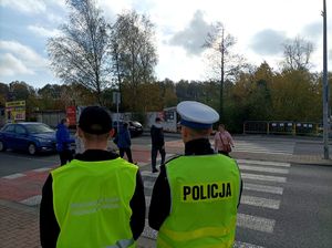 Zdjęcie kolorowe przedstawiające ucznia klasy mundurowej oraz policjanta przy przejściu dla pieszych.