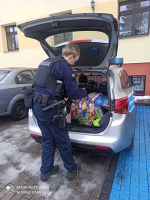 Zdjęcie przedstawiające policjantkę wraz z zebranymi podarunkami dla dzieci, w tle widać radiowóz.