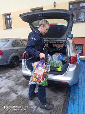 Zdjęcie przedstawiające policjantkę wraz z zebranymi podarunkami dla dzieci, w tle widać radiowóz.