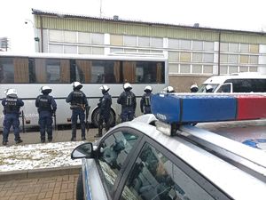 Zdjęcie przedstawiające policjantów, część radiowozu policyjnego oraz autobus.