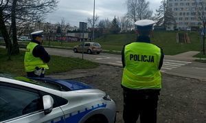 Zdjęcie przedstawiające dwóch policjantów i radiowóz.