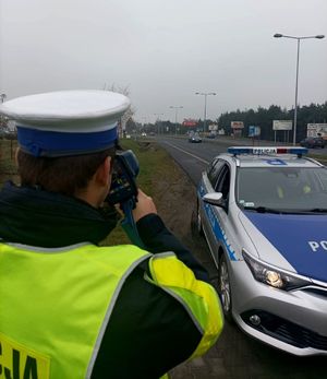 Zdjęcie przedstawiające policjanta w trakcie mierzenia prędkości na urządzeniu do pomiaru prędkości.