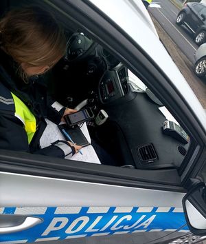 Zdjęcie przedstawiające policjntkę sprawdzającą dokumenty kierowcy.