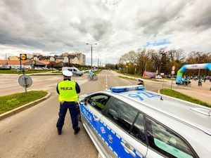 Zdjęcie przedstawiające radiowóz policyjny oraz policjantów zabezpieczających przejazd rowerzystów.