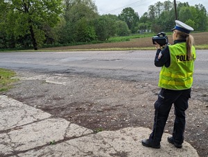 Zdjęcie przedstawiające policjantkę trzymającą radar i dokonującą pomiar prędkości.