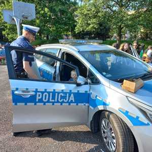 Zdjęcie przedstawiające policjanta, radiowóz oraz uczestników festynu.