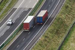 Zdjęcie przedstawiające autostradę oraz dwa samochody ciężarowe oraz jeden samochód osobowy.