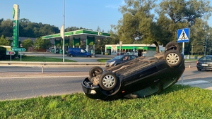 Na zdjęciu widoczny pojazd osobowy leżący na dachu przed przejściem dla pieszych. W tle widoczna stacja paliw.