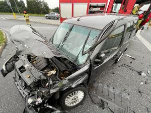 zdjęcie przedstawiające uszkodzony czarny samochód biorący udział z zdarzeniu drogowym oraz samochód Państwowej Straży Pożarnej