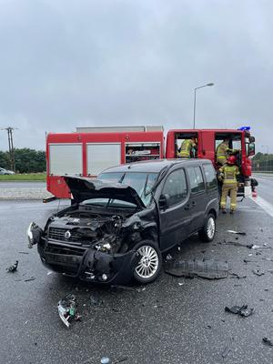 zdjęcie przedstawiające uszkodzony czarny samochód biorący udział z zdarzeniu drogowym oraz samochód Państwowej Straży Pożarnej