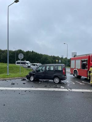 zdjęcie przedstawiające uszkodzony czarny samochód biorący udział z zdarzeniu drogowym oraz samochód Państwowej Straży Pożarnej