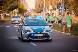Zdjęcie przedstawiające policjanta, uczestników oraz radiowóz w trakcie zabezpieczenia.