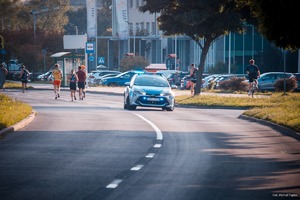 Zdjęcie przedstawiające radiowóz w trakcie zabezpieczenia oraz osoby przygotowujące się do biegów.