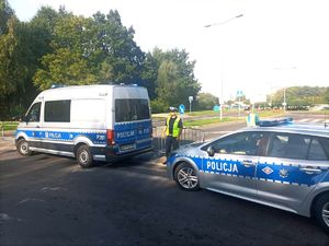 Zdjęcie przedstawiające policjanta oraz dwa radiowozy w trakcie zabezpieczenia.