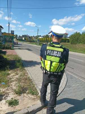 Zdjęcie kolorowe przedstawiające policjanta ruchu drogowego stojącego przy jezdni, obserwującego poruszające się pojazdy.