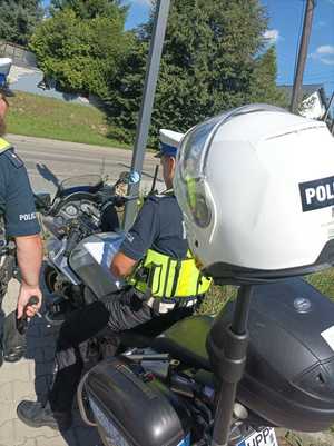 Zdjęcie kolorowe przedstawiające policjantów ruchu drogowego oraz policyjny motocykl.