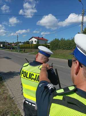 Zdjęcie kolorowe przedstawiające policjantów ruchu drogowego w trakcie pracy na urządzeniu do pomiaru prędkości.